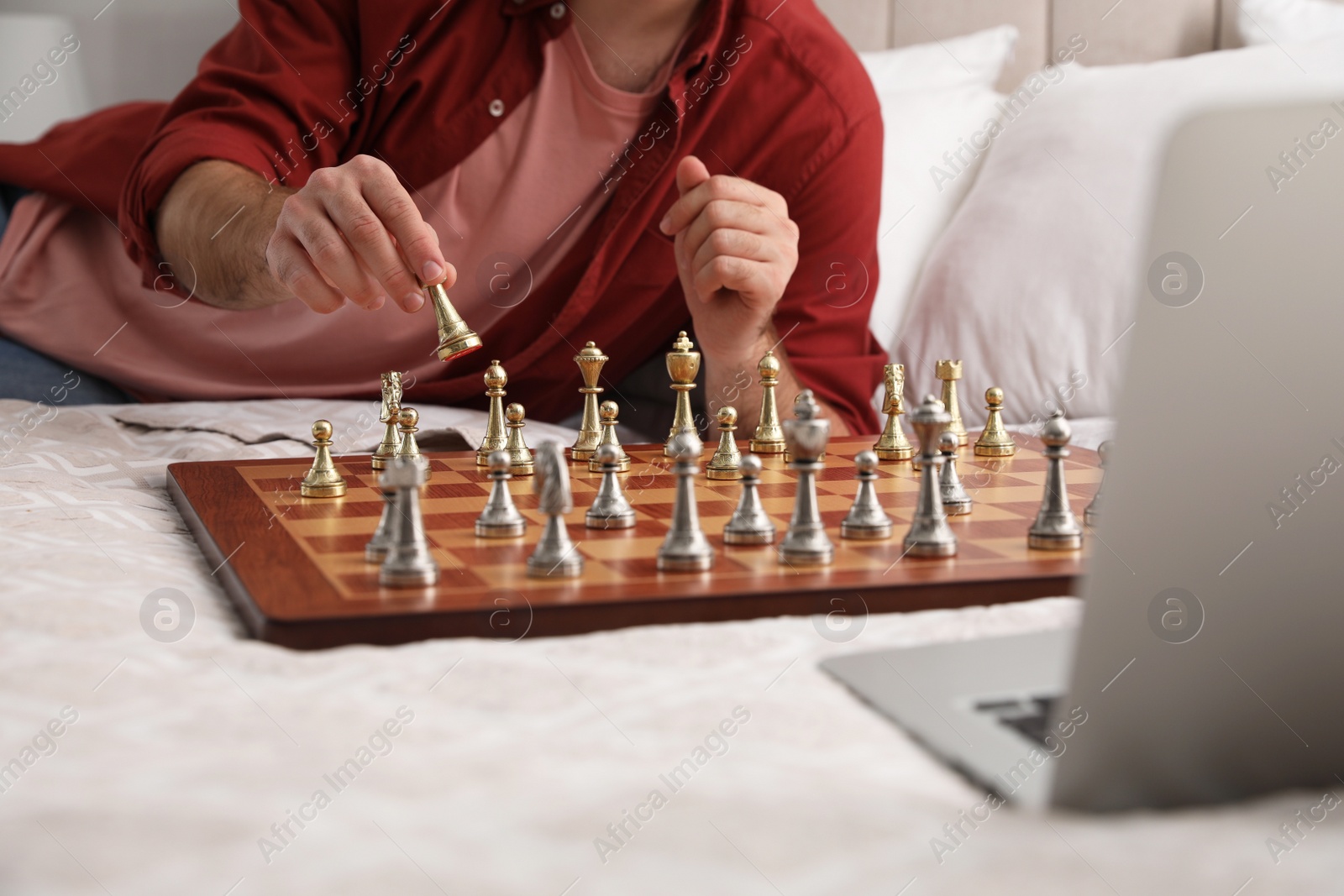 Photo of Man playing chess with partner through online video chat on bed, closeup