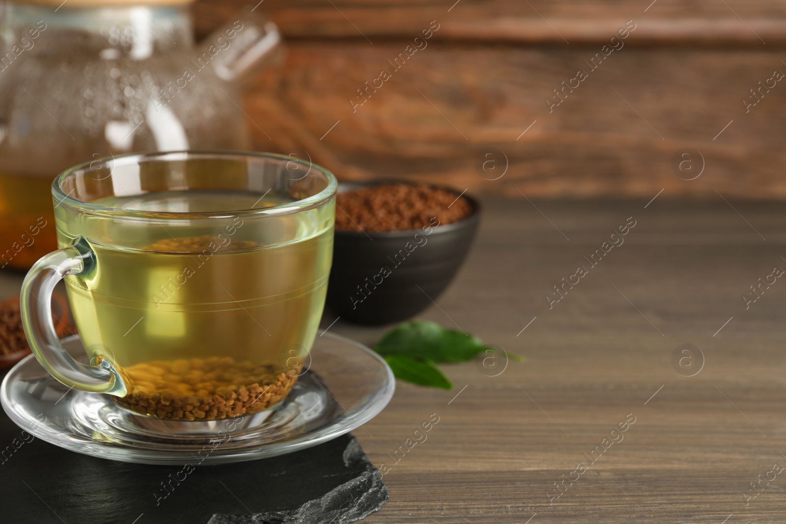 Photo of Freshly made buckwheat tea in glass cup on wooden table. Space for text