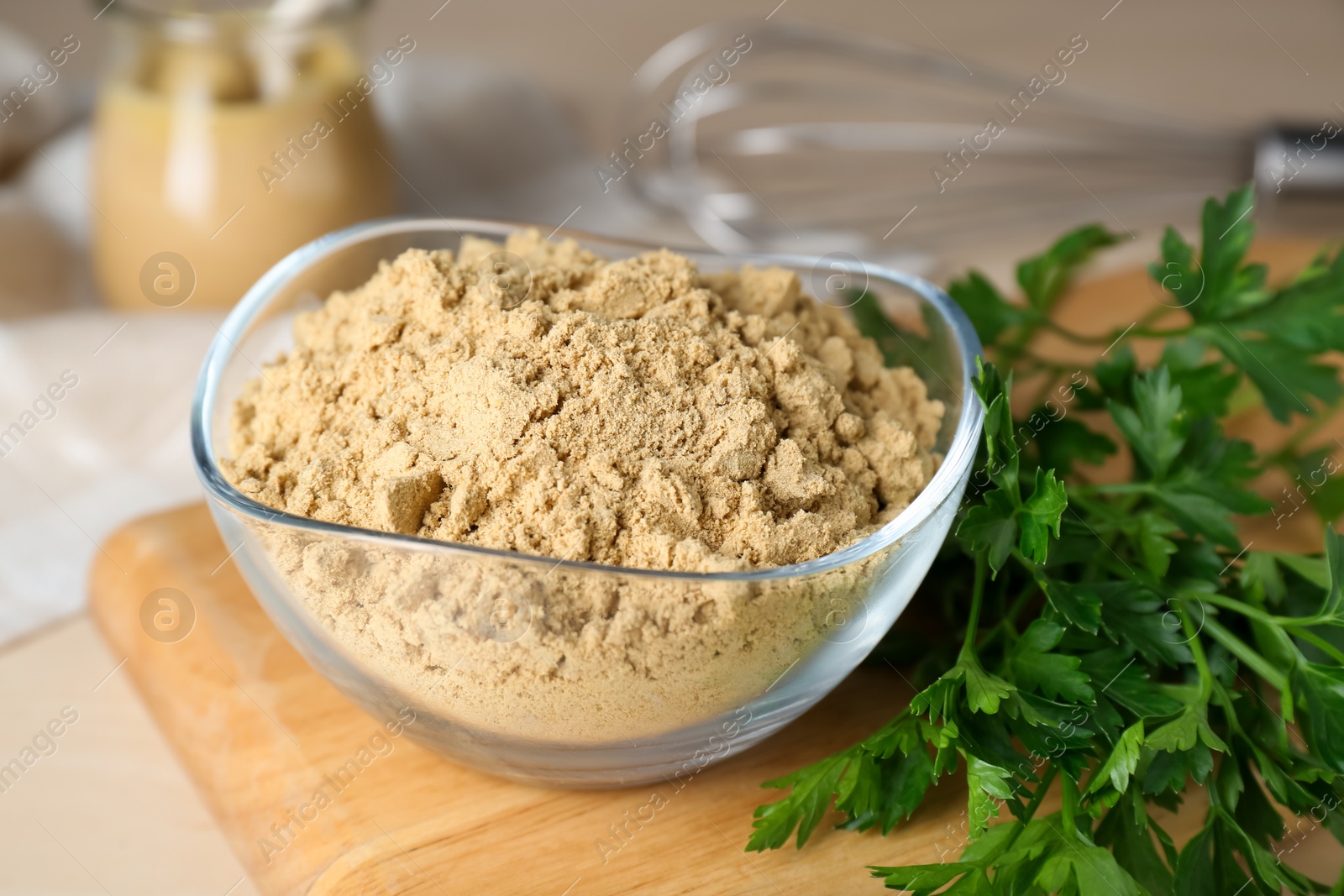 Photo of Bowl of aromatic mustard powder and parsley on wooden table, closeup