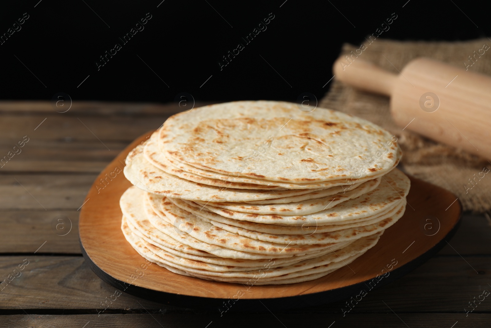 Photo of Many tasty homemade tortillas and rolling pin on wooden table