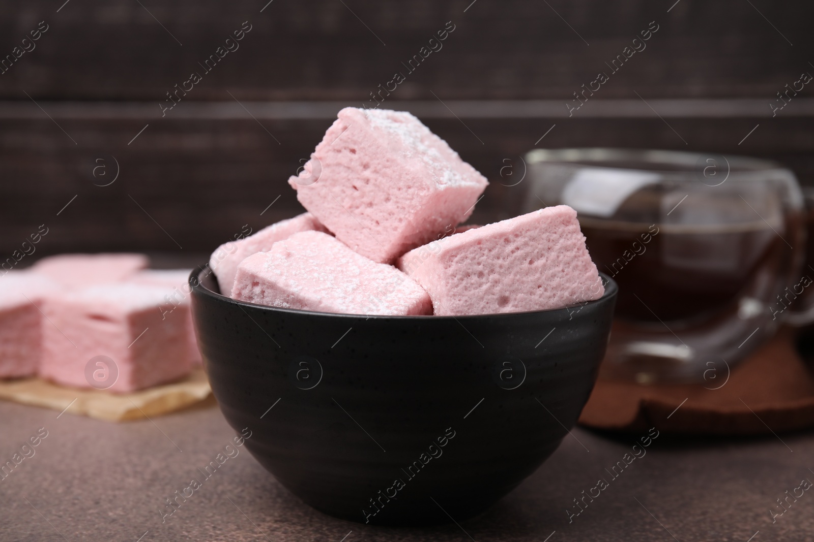 Photo of Bowl of delicious sweet marshmallows with powdered sugar on brown table, closeup