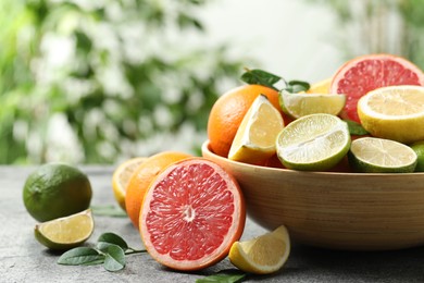 Photo of Different fresh citrus fruits and leaves on grey table against blurred background, closeup