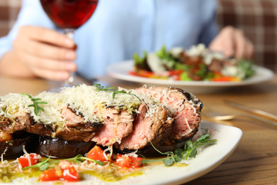 Photo of Delicious roasted meat and blurred woman on background, closeup