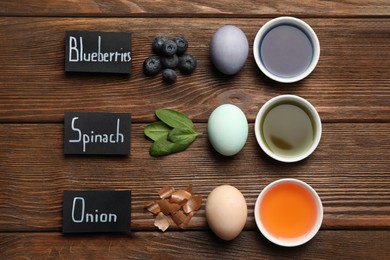 Photo of Easter eggs painted with natural organic dyes and labels on wooden table, flat lay. Blueberries, spinach, onion used for coloring