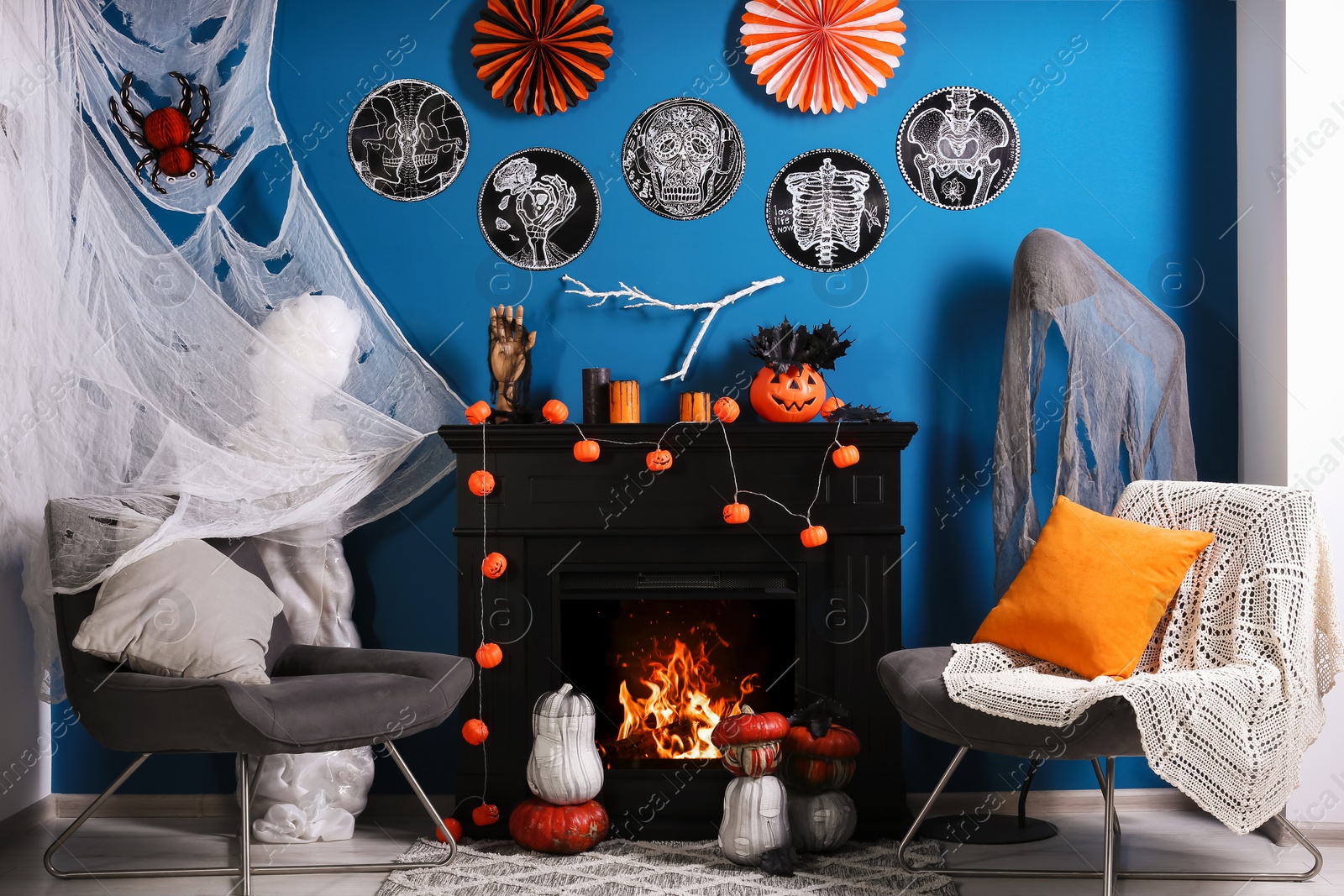 Photo of Jack-o'-lanterns and different Halloween decorations on black fireplace near blue wall