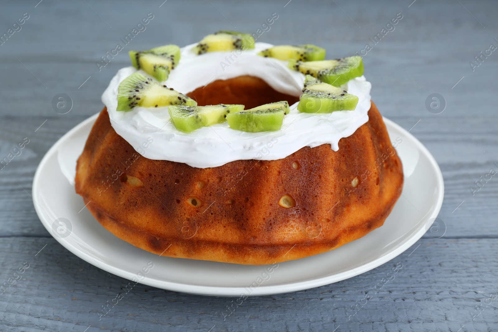 Photo of Homemade yogurt cake with kiwi and cream on grey wooden table