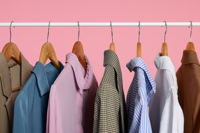 Photo of Rack with stylish clothes on wooden hangers against pink background, closeup