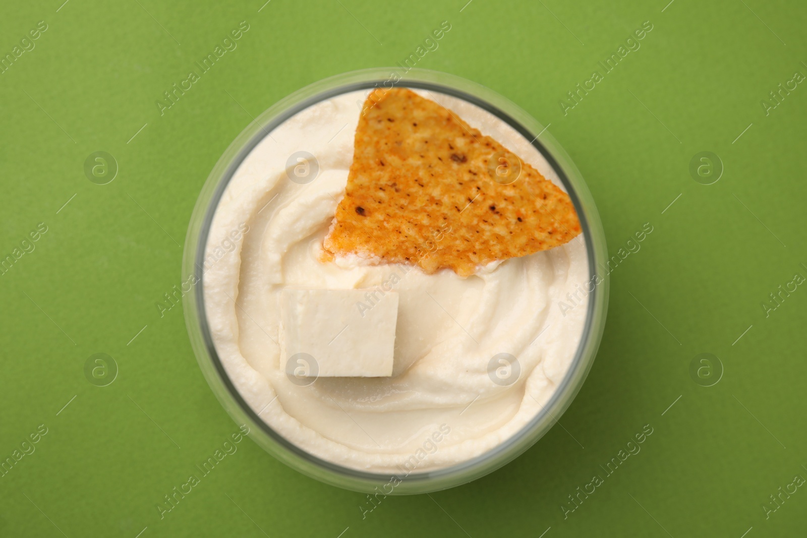 Photo of Delicious tofu sauce served with nachos chip on green background, top view