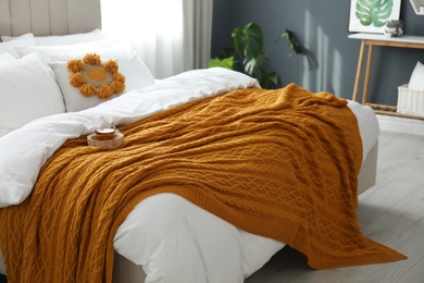 Cup of tea and knitted orange plaid on bed in stylish room interior