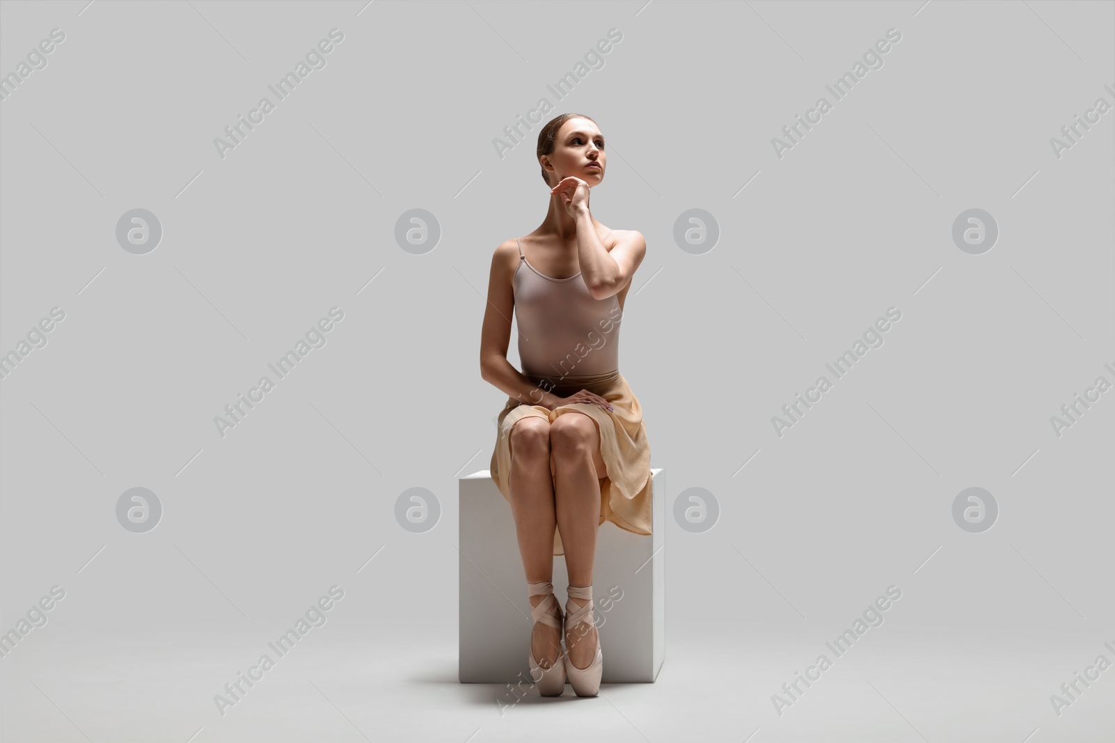 Photo of Young ballerina practicing dance moves on cube against white background