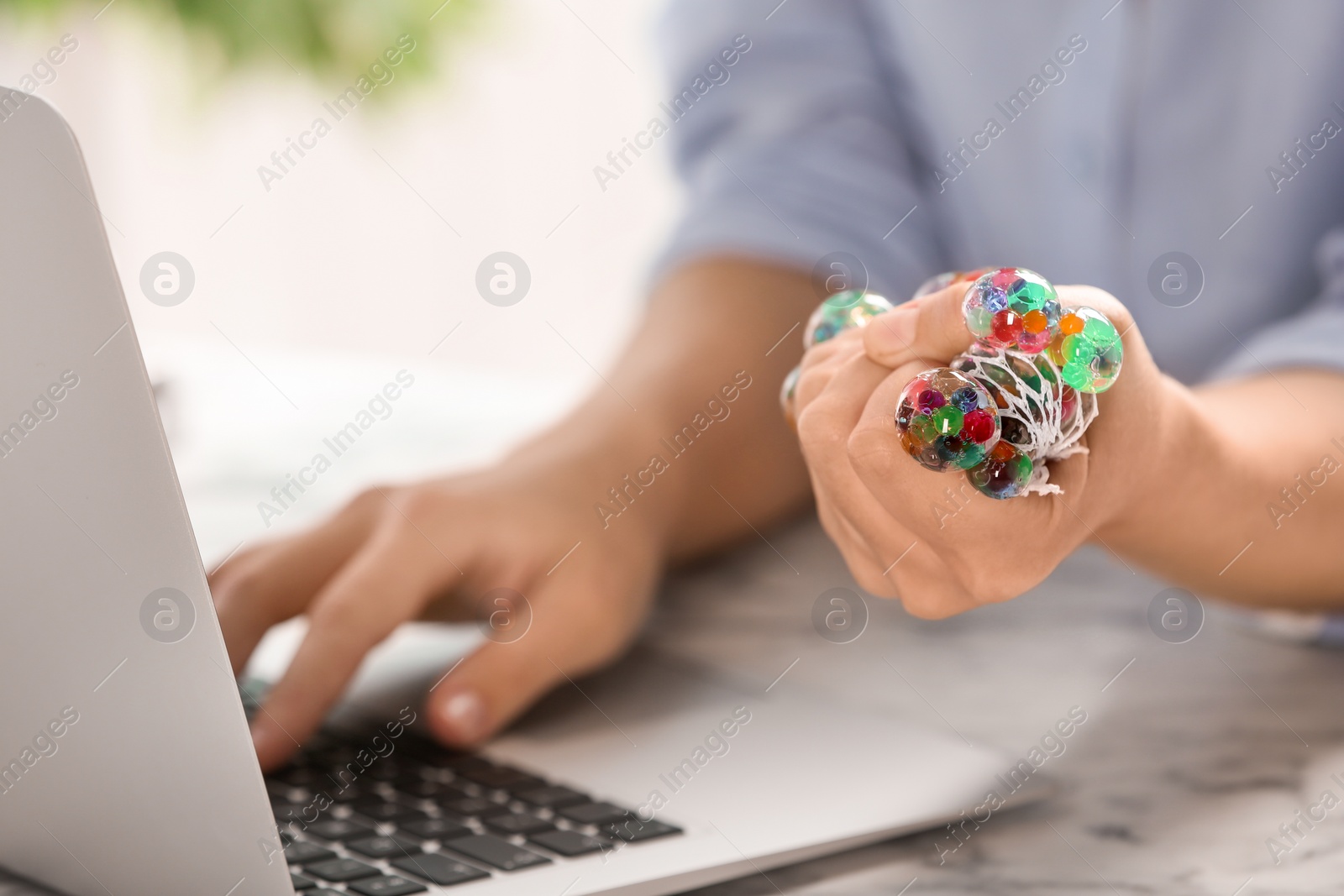 Photo of Woman squeezing colorful slime in office, closeup. Antistress toy