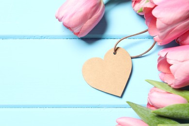 Happy Mother's Day. Beautiful pink tulips and blank heart shaped card on light blue wooden table, flat lay. Space for text