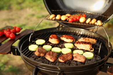 Photo of Modern grill with meat and vegetables outdoors, closeup. Camping cookout