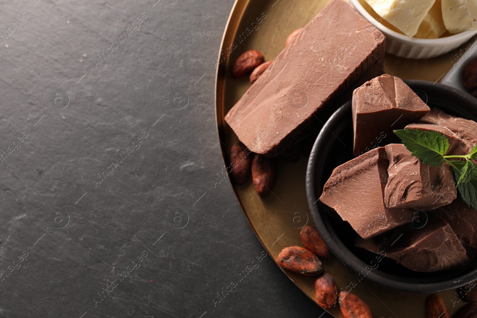 Photo of Pieces of tasty chocolate, mint and cocoa beans on black table, top view. Space for text