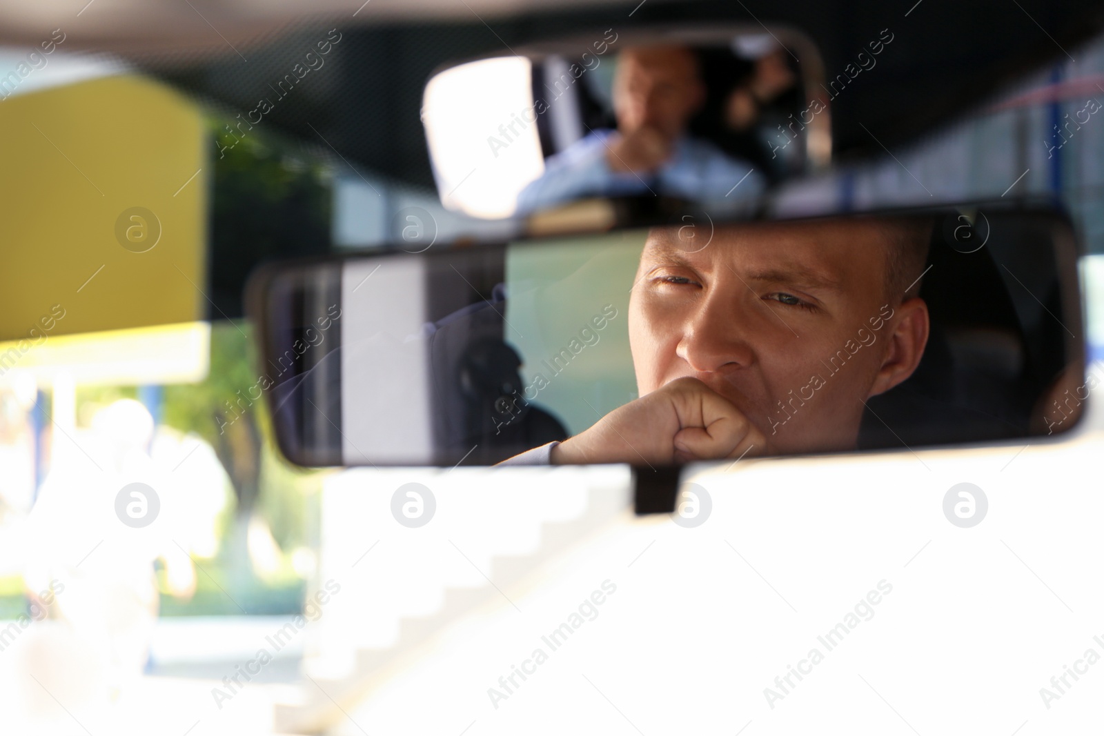 Photo of Tired young man yawning in his car, view through rear mirror