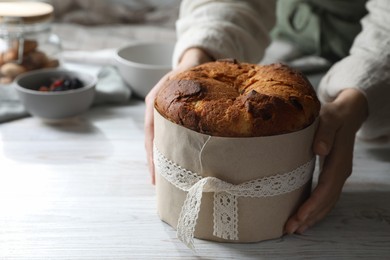 Photo of Woman holding delicious Panettone cake at white wooden table, closeup and space for text. Traditional Italian pastry
