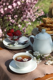 Beautiful spring flowers, freshly baked waffles and ripe strawberries on table served for tea drinking in garden
