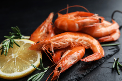 Photo of Delicious cooked shrimps with lemon and rosemary on black table, closeup