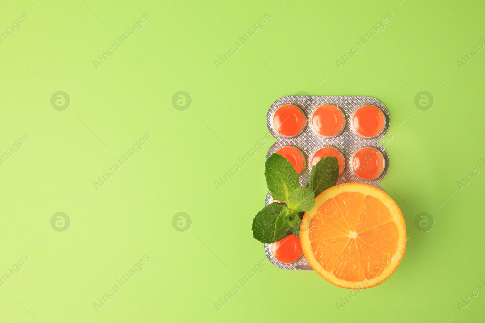 Photo of Fresh orange, mint leaves and blister with cough drops on light green background, flat lay. Space for text
