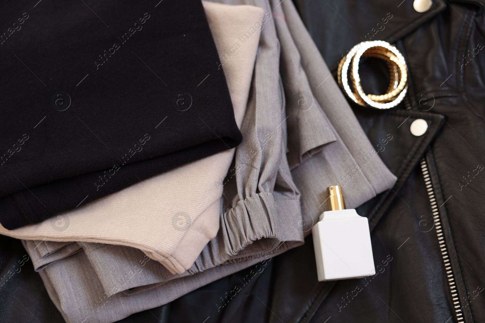 Photo of Folded clothes, bracelets, bottle of perfume and black leather jacket , flat lay