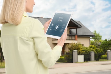 Woman using smart home control system via tablet near house outdoors, closeup