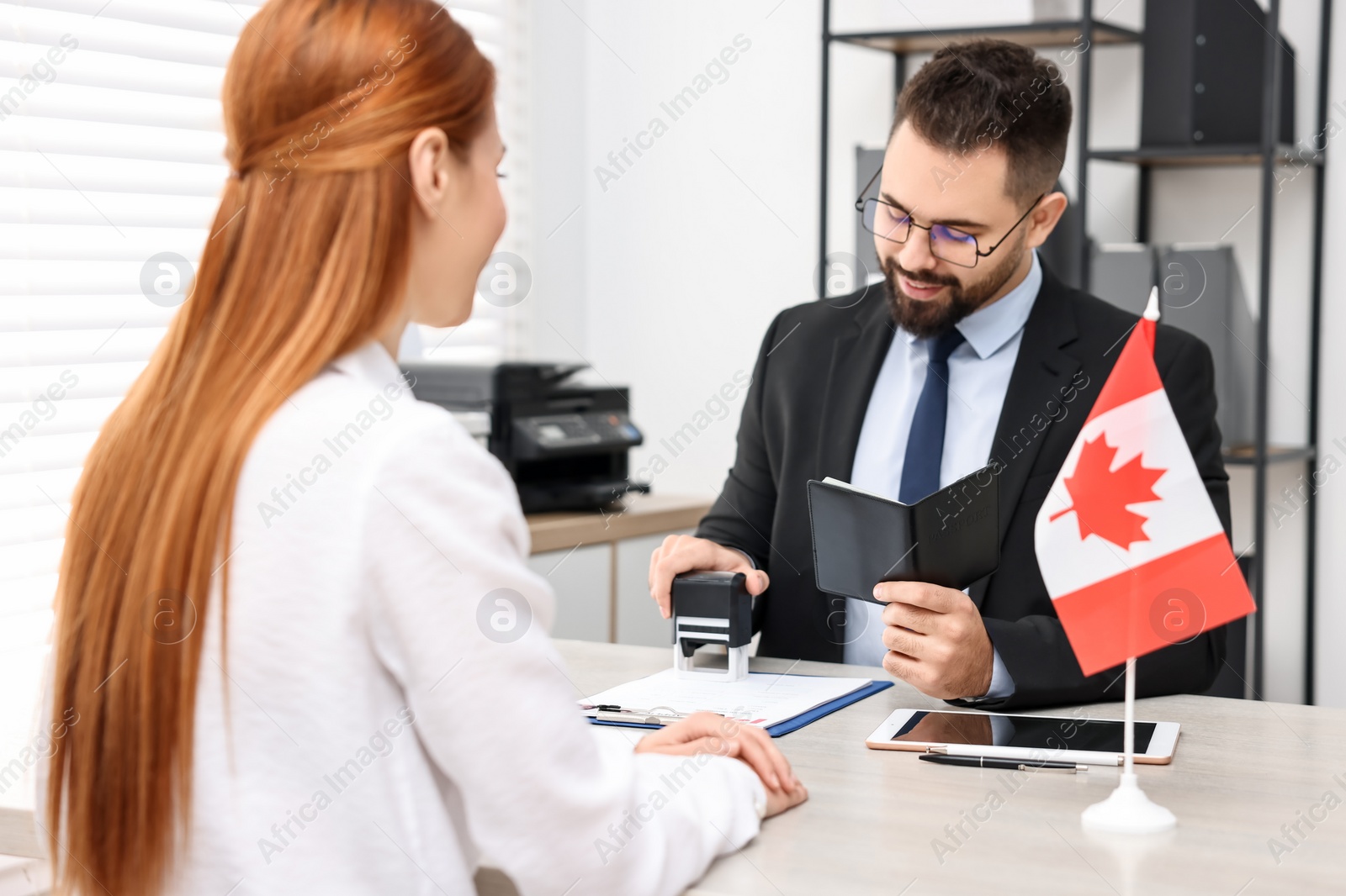 Photo of Immigration to Canada. Smiling embassy worker approving woman's visa application form in office