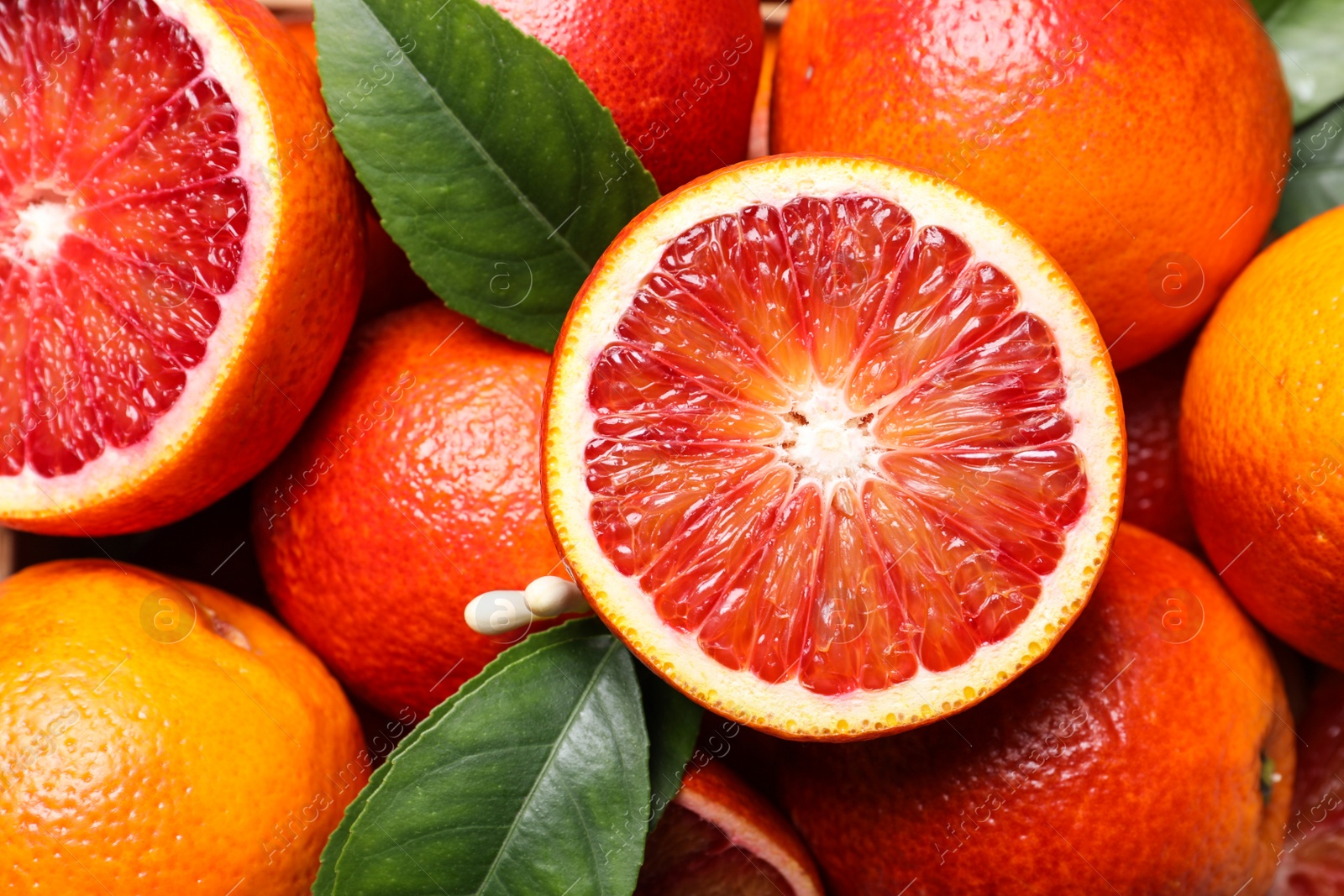 Photo of Whole and cut ripe red oranges with green leaves, closeup