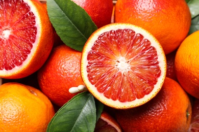 Photo of Whole and cut ripe red oranges with green leaves, closeup