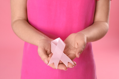 Photo of Woman holding pink ribbon on color background, closeup. Breast cancer awareness