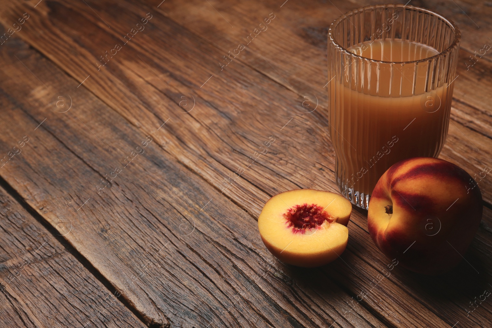 Photo of Glass of peach juice and fresh fruits on wooden table. Space for text