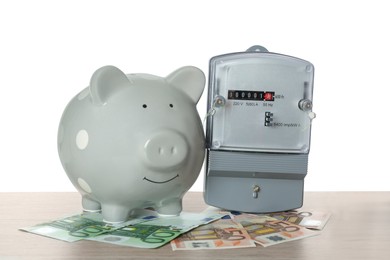 Photo of Electricity meter, piggy bank and money on wooden table against white background