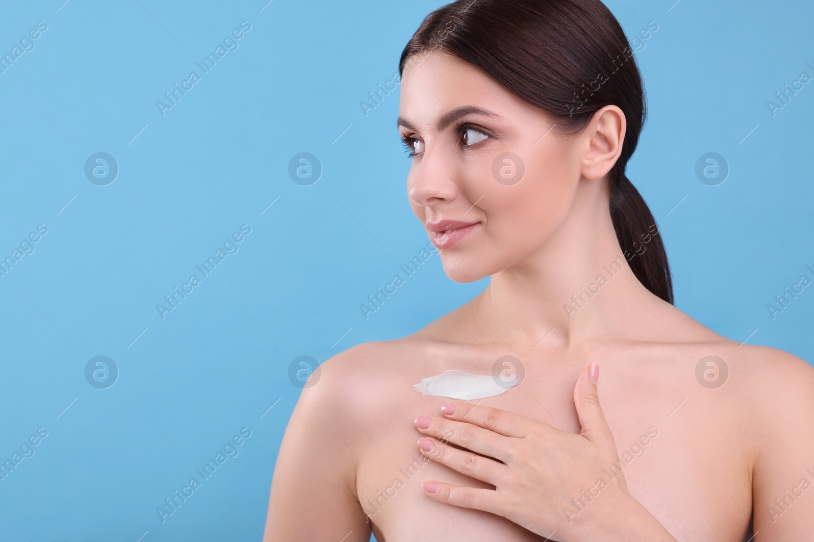 Photo of Beautiful woman with smear of body cream on her collarbone against light blue background, space for text