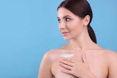 Beautiful woman with smear of body cream on her collarbone against light blue background, space for text