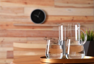 Photo of Tray with jug and glasses of water on wooden table in room, space for text. Refreshing drink