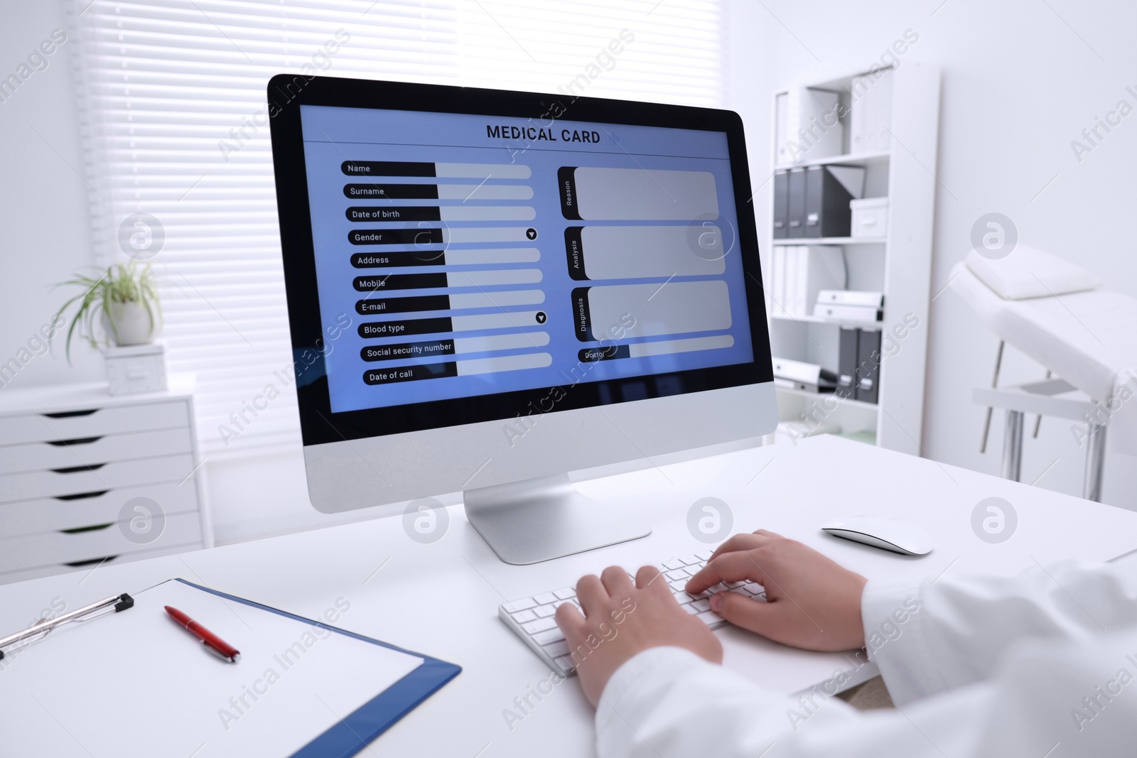 Photo of Doctor using computer to fill out patient's medical card at table in clinic, closeup