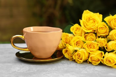 Photo of Cup of drink and beautiful yellow roses on light table outdoors