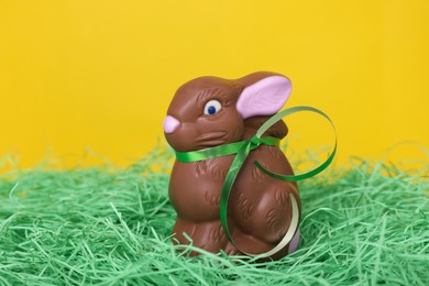 Photo of Easter celebration. Cute chocolate bunny on grass against yellow background