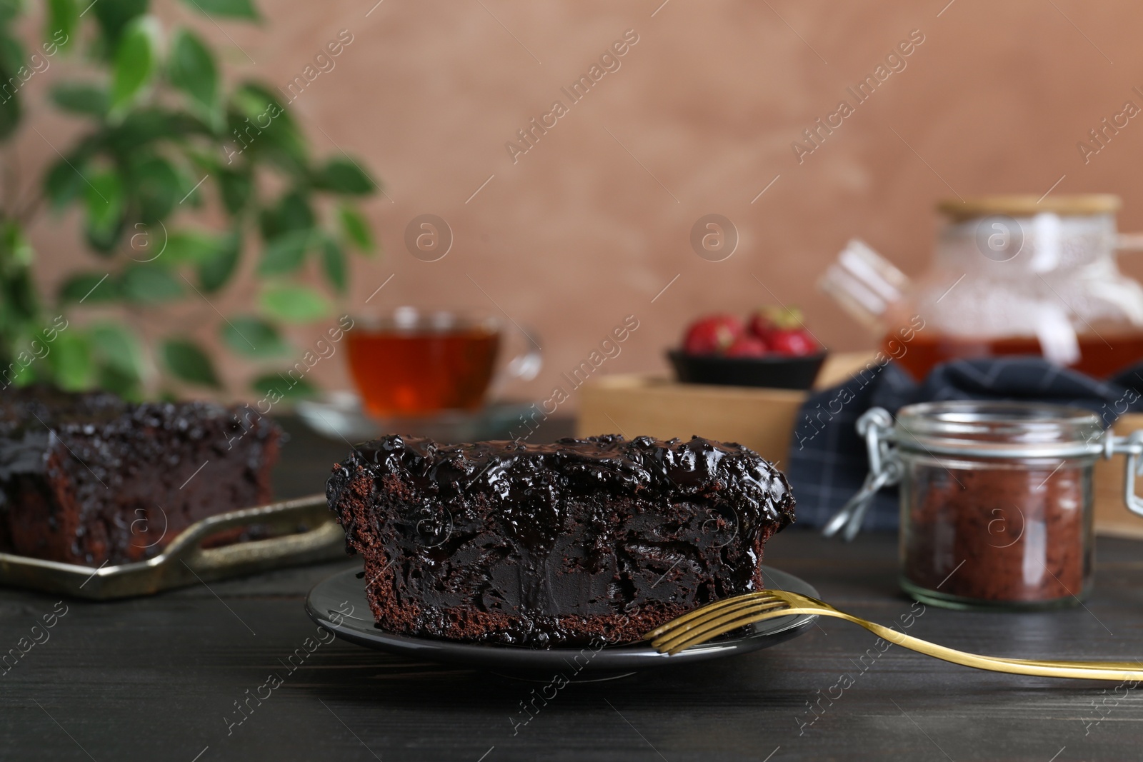Photo of Piece of tasty chocolate sponge cake on black wooden table