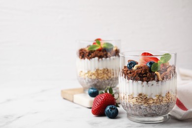 Photo of Tasty granola with berries, nuts, yogurt and chia seeds in glasses on white marble table, space for text