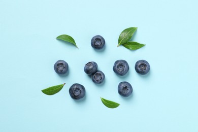 Tasty fresh blueberries with green leaves on light blue background, flat lay