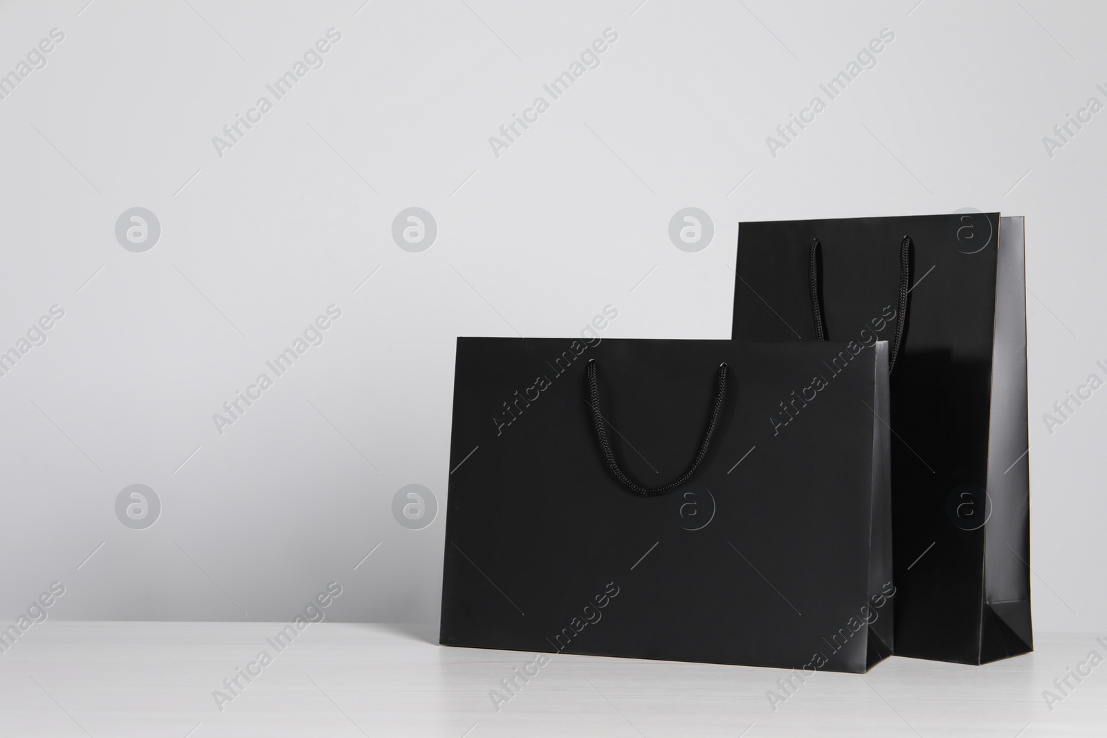 Photo of Black paper bags on white wooden table, space for text