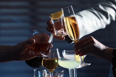 People with different alcohol drinks clinking glasses indoors, closeup