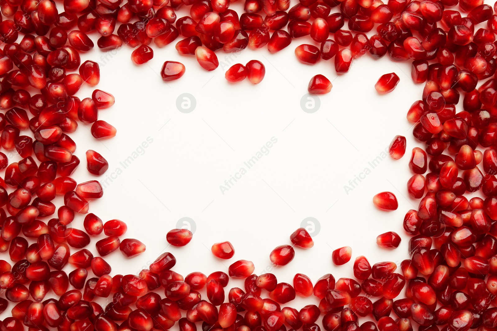 Photo of Frame made of ripe juicy pomegranate grains on white background, top view. Space for text