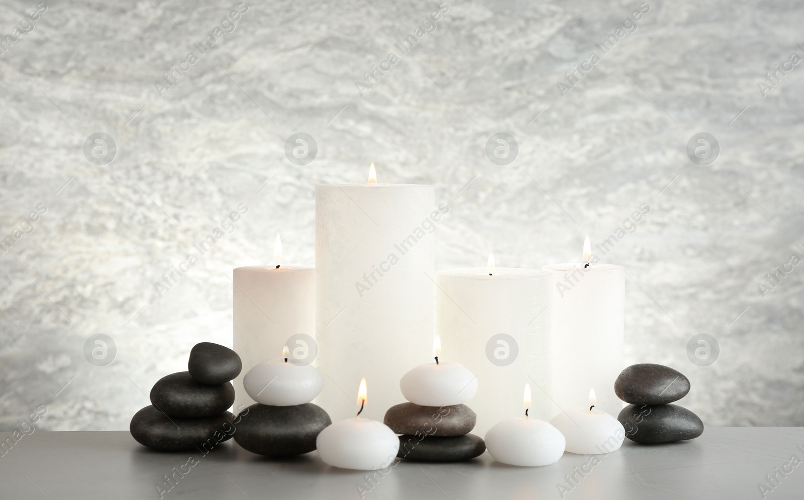 Photo of Beautiful composition with candles and stones on table against light background