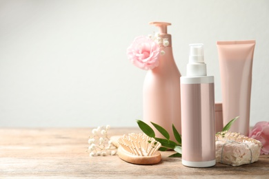 Set of hair cosmetic products, brush and flowers on wooden table against white background. Space for text