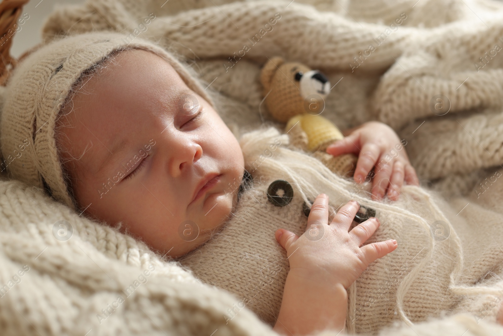 Photo of Adorable newborn baby with toy bear sleeping on knitted plaid, closeup