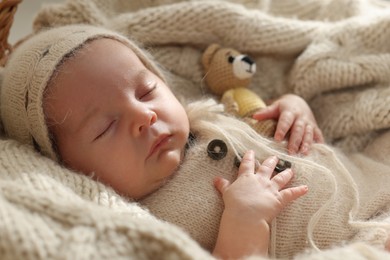 Adorable newborn baby with toy bear sleeping on knitted plaid, closeup