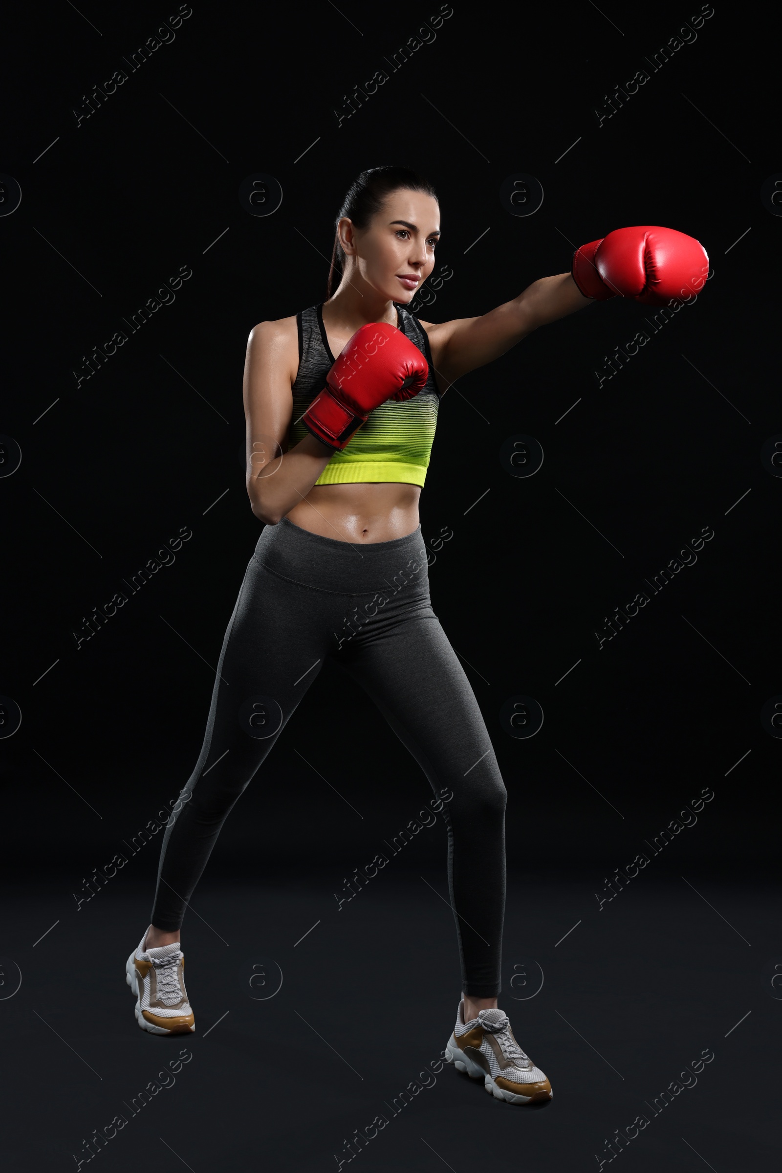 Photo of Beautiful woman in boxing gloves training on black background