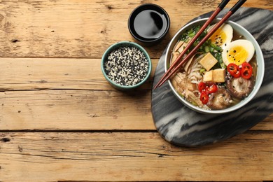 Photo of Noodle soup. Bowl of delicious ramen and chopsticks on wooden table, flat lay. Space for text