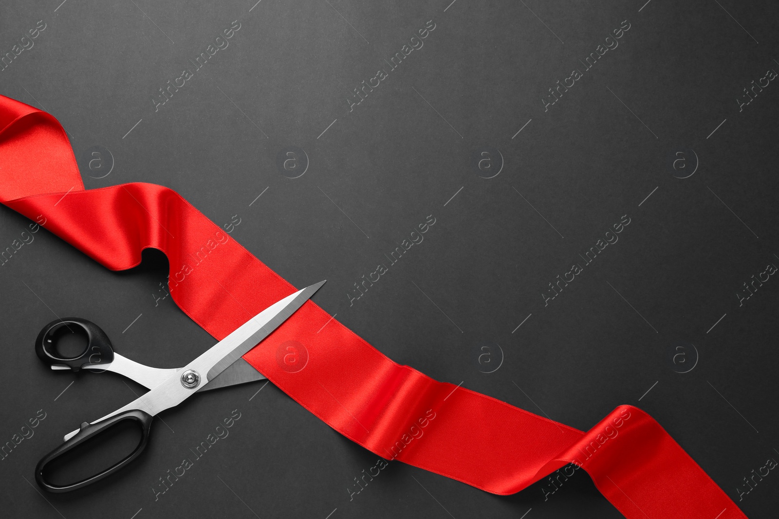 Photo of Red ribbon and scissors on black background, top view. Space for text